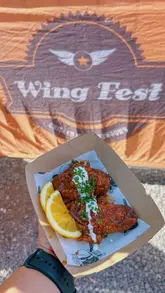 A fast-paced montage video showcasing the Wing Fest UK festival, featuring various chicken wing stalls, live music, and close-up shots of different wing dishes being sampled by attendees.
