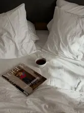 A clean, aspirational lifestyle shot of a hotel bed featuring a cup of coffee and a magazine, used to promote a stay at the Hyatt Regency London Blackfriars.