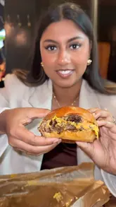 A short video featuring a creator trying the smashed onion double cheeseburger at Flat Iron, followed by a shot of a steak being drizzled with sauce.