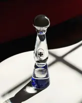 A high-quality, professional product shot of a Clase Azul tequila bottle placed on a marble surface. The lighting is dramatic and intentional, highlighting the unique shape and texture of the hand-blown ceramic decanter against a dark, moody background.