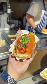 A food influencer reviews the 'Bong Dogz' collaboration pop-up at the CelebrAsia event at Battersea Power Station, showcasing the menu items including the 'Dreamz Dog' and 'Bonganissa Cheeseburger'.