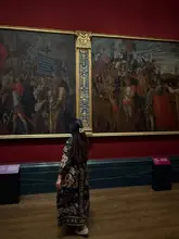 A high-quality, atmospheric shot of a visitor standing in front of large, classical paintings within the National Gallery. The composition is balanced and the lighting respects the gallery environment, creating a sophisticated and contemplative mood.