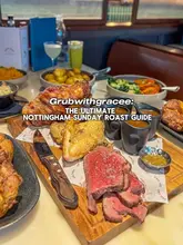 A high-angle, appetizing shot of a Sunday roast spread, including sliced beef, roast potatoes, vegetables, and gravy boats, presented on a wooden board.