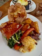 A top-down, overhead shot of a Sunday roast dinner served at a pub, featuring pork belly, a large Yorkshire pudding, roast potatoes, and vegetables.