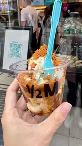 A short, punchy promotional video for Half Million cafe in London, focusing on their viral 'Coffee Crunch' dessert. The video features close-up shots of the preparation, including pouring espresso and sauces over ice cream, followed by a shot of the creator enjoying the treat outside the venue.