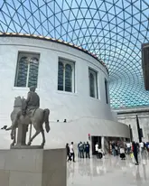 A clear, wide-angle photograph of the Great Court at the British Museum, showcasing the iconic glass roof architecture and the central statue.