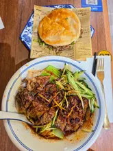 A top-down, overhead shot of a meal at Q-beef noodles in Soho, featuring a bowl of beef rib noodles and a Chinese burger (roujiamo) served on branded paper.