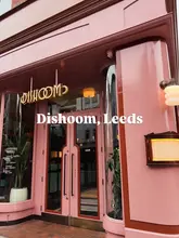 A clean, eye-level exterior shot of the Dishoom restaurant in Leeds, showcasing its distinctive pink facade and branding.