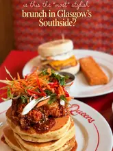A high-quality, close-up shot of a stack of pancakes topped with fried chicken and slaw, with a breakfast muffin and hash brown visible in the background, set in a diner-style environment.