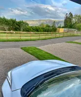 A scenic, point-of-view shot taken from inside a vehicle, showcasing a picturesque campsite in the Lake District with a stunning mountain backdrop. The image captures the peaceful, outdoor atmosphere of the location.