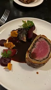 A montage showcasing a high-end dining experience at One Devonshire Gardens, featuring tableside carving of a Beef Wellington, bread service, scallops, tomato salad, and dessert.