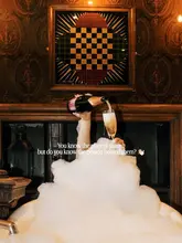 A highly stylized, atmospheric lifestyle shot featuring a person in a bubble bath holding a glass of champagne, set against a dark, moody interior with a fireplace. The image uses warm, intentional lighting to create a luxurious and relaxing aesthetic.