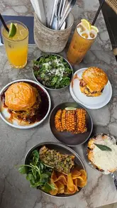 A high-quality, fast-paced montage showcasing a variety of dishes at Burger & Beyond, including burgers, steak tartare, corn ribs, and dessert, with close-ups of food preparation and consumption.