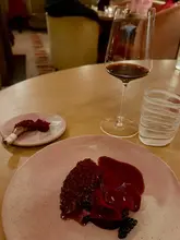 A sophisticated, moody close-up shot of a pigeon dish served with beetroot and blackberry, paired with a glass of red wine at the three-Michelin-starred Hélène Darroze at The Connaught. The image captures the essence of high-end fine dining with elegant plating and atmospheric lighting.