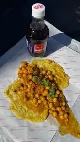 A review of Moto Roti in Acton, featuring a variety of Trinidadian street food dishes like doubles, bakes, and goat roti. The creator provides context on the dishes and highlights the freshness of the preparation.