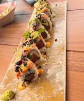 A close-up, high-angle shot of a long, rectangular plate of spicy tuna sushi rolls served on a wooden table, likely at a rooftop venue.