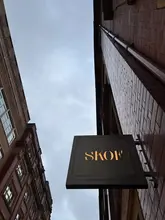 A low-angle, sharp shot of the 'SKOF' restaurant sign against a grey, overcast sky, capturing the exterior of the Michelin-starred venue in Manchester.
