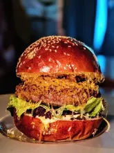 A high-quality, close-up, eye-level shot of a gourmet burger, showcasing distinct layers of ingredients including a patty, melted cheese, lettuce, and black pudding, served on a toasted brioche bun.