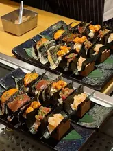 A high-quality, close-up shot of an array of Japanese dishes, specifically sushi and donburi, arranged neatly on wooden stands. The lighting highlights the textures of the fish, wagyu, and toppings like caviar and truffle, creating an inviting and premium aesthetic suitable for a fine dining restaurant setting.