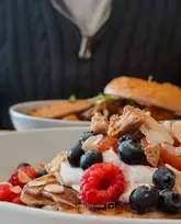 A close-up, appetizing shot of fruit-topped pancakes at Parx Café, with a blurred background featuring a person in a black sweater.