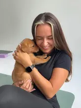 A high-quality, well-lit portrait of a woman holding a puppy during a puppy yoga session, capturing a joyful and engaging moment.