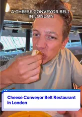 A short, punchy video showcasing a unique cheese conveyor belt restaurant in London. The creator highlights the experience of picking plates off the belt and reviews specific items, including a standout whipped goat's cheese doughnut.