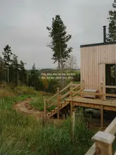 A beautifully composed, atmospheric shot of a wooden cabin retreat nestled in a rural landscape. The image uses natural, overcast lighting to create a moody, inviting aesthetic that perfectly captures the 'escape' nature of the venue. The composition is strong, with the path leading the eye toward the cabin, and the technical quality is high with sharp focus and good resolution.