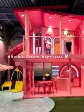 A montage of a visit to the Barbie Dream Experience in Amsterdam, featuring the daughter exploring various themed rooms, interactive exhibits, and the pink-themed cafe.