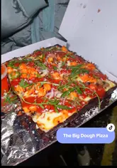 A creator reviews a Detroit-style pizza takeaway service called 'Big Dough' in Hamilton. The video features the creator ordering via an app, followed by a close-up taste test of a chicken tikka pizza and a pepperoni pizza, along with wings and fries, highlighting the quality of the crust and toppings.
