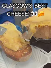 A short, energetic vlog-style review of Cheese Box Glasgow, a street food stall operating out of a converted police box. The video features the creator trying various cheese-based dishes, including raclette and a cheese baguette, while highlighting the unique outdoor seating area and the friendly service.