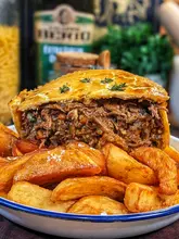 A beautifully baked Guinness Beef & Blue Cheese Pie with a golden, flaky crust, served with a side of crispy chunky chips.
