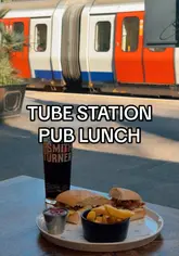 A short video showcasing a pub located right next to a London Underground station, featuring a view of the trains passing by while the creator enjoys a lunch of a sandwich, fries, and a pint.