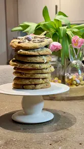 Pile of Easter Mini Egg choc chip cookies drizzled with chocolate fudge icing and decorated with pastel mini eggs.