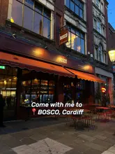A night-time exterior shot of the Bosco Pizzeria & Trattoria in Cardiff, showcasing the restaurant's inviting facade and outdoor seating area.