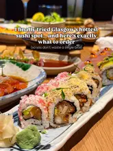 A high-quality, close-up shot of a sushi platter at a restaurant, featuring various rolls with garnishes, with a blurred background of other dishes.