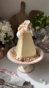 A visually polished recipe tutorial demonstrating the creation of a ricotta-based Easter Paskha with caramel filling, showcasing the preparation process from blending ingredients to the final assembly and decoration.