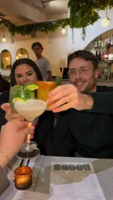 A creator visits Roots in Upminster, highlighting the venue's transition from brunch by day to pizza by night. The video features a variety of cocktails, including a chili mango margarita and light martini, alongside dishes like pizza, a smash burger, chicken caesar salad, and sides such as padron peppers and garlic bread. The creator and friends are shown enjoying the food and atmosphere.