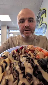 A creator reviews a large acai bowl from Harvest Jack's in Bangor, highlighting its size and price point. The video features the creator talking to the camera, interspersed with close-up shots of the bowl being prepared and eaten.