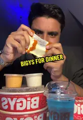The video features a creator reviewing several menu items from a takeaway spot called Bigys. The creator samples a cheese-filled item, mac and cheese, a burger, and honey chicken with rice, providing commentary and ratings for each. The video is filmed in a static, mukbang-style format with the creator sitting at a table.