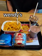Wendy's Baconator, spicy chicken sandwich, cheese fries, and Frosty drinks on a table in Glasgow city centre.