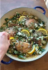 Close-up of a one-pan lemon oregano chicken and giant couscous dish with olives, spinach, feta, and parsley.