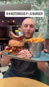 Juicy NOTORIOUS P.I.G Burger with double cheese, double bacon, pork belly, BBQ pulled pork, bacon jam, hot honey, and sausage.