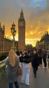Tourists strolling along the South Bank of the River Thames, with the London Eye and Houses of Parliament in the background.