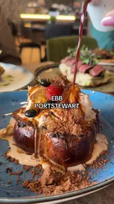 A review of Ebb Coffee in Portstewart, highlighting their brunch menu, including avocado toast, a steak sandwich, duck waffle, and French toast, alongside their unique 'split cup' drinks. The video features the creator trying the food and drinks, showing the menu, and capturing the cafe's interior and sea views.