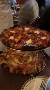 A short, rhythmic montage showcasing a pizza restaurant in London. The video features quick cuts of the venue's entrance, table settings, and close-ups of their signature pizzas, including a pesto-swirled pie and a pepperoni option.