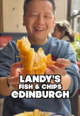 Here are a few options for your alt text, depending on the specific focus of the image:

**Option 1 (Focus on the meal):**
Crispy haddock, chunky chips, and a pizza crunch served at Landy’s Fish and Chips on the Royal Mile in Edinburgh.

**Option 2 (Focus on the shop/location):**
Landy’s Fish and Chips shop on North Bridge, Edinburgh, serving traditional Scottish fish suppers and pizza crunches.

**Option 3 (Short & punchy):**
A classic Scottish fish and chip meal with a pizza crunch from Landy’s Fish and Chips on the Edinburgh Royal Mile.