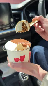 A short, handheld clip showcasing a tiramisu cookie being scooped with a wooden spoon inside a car.