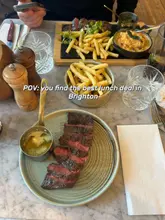 A POV-style overhead shot of a steak and fries lunch deal served on a marble table, featuring a side dish and drinks.