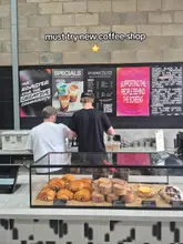 A shot taken at the counter of Studio Black Coffee, highlighting their pastry selection in a glass display case with the menu and staff in the background.
