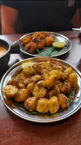 A close-up, eye-level shot of a plate of gunpowder potatoes, with a plate of chicken tikka and a person's arm visible in the background.